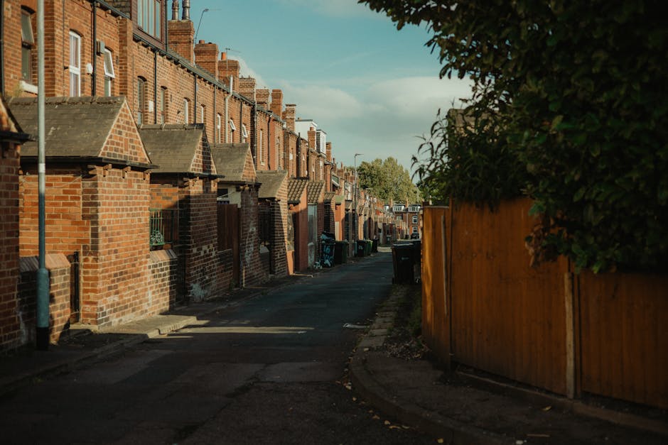 An outdoor view of a residential housing area featuring a row of modern, neatly maintained houses with white painted exterior walls and brown tiled roofs. The scene includes a well-kept garden with lu